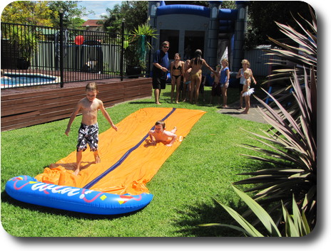 Two youngsters sliding along yellow plastic slide on lawn