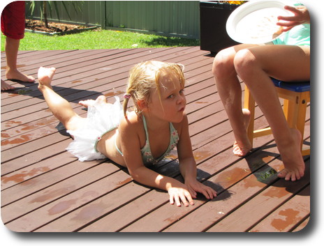 Little girl, wet from being in the pool, laying belly down on the wooden deck