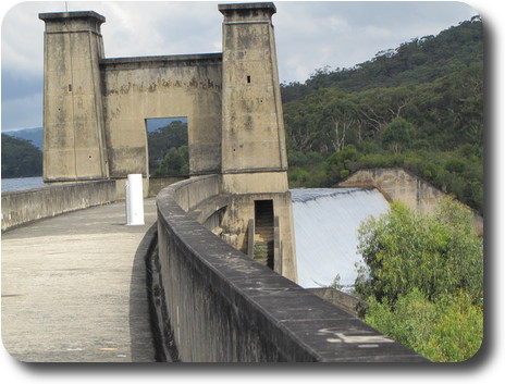 End of curving wall, concrete arch and spillway with water beyond