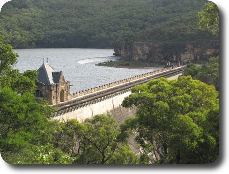 Concrete dam, straight wall, crenellated top and semi-circular spillway at far end