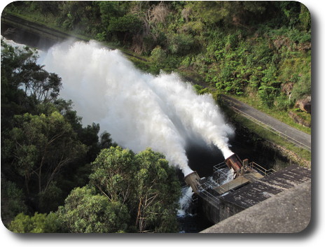 A pair of metal tubes at base of dam; a stream of water coming from both tubes