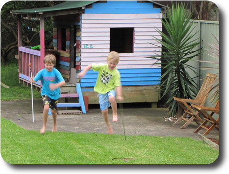 Two little boys in back yard, in front of blue and white cubby house