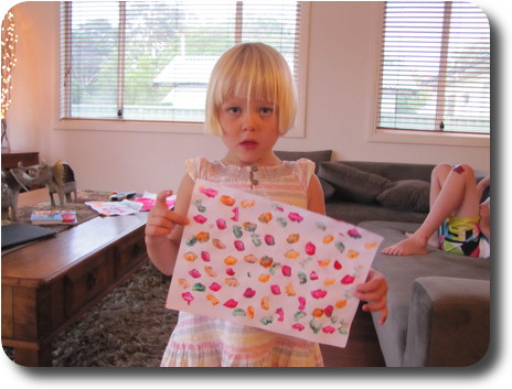 Little girl with piece of paper on which are her coloured thumb prints