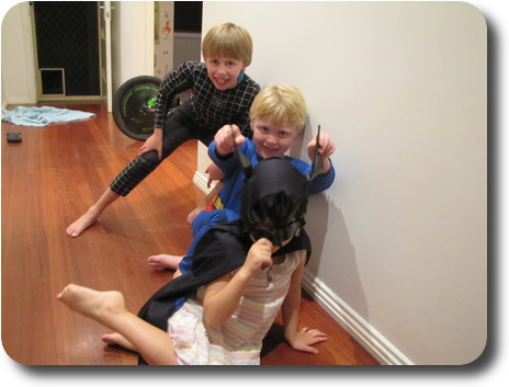 Little boy as Spiderman behind little boy as Superman behind little girl as Batman in hallway