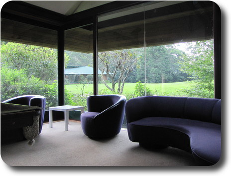 Room with purple lounge and chairs, large windows looking out to lawn and main house