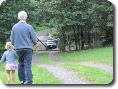 Man and little girl, backs to camera, walking to gate with car waiting to enter