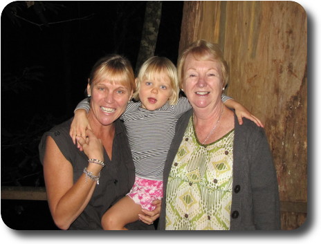 Two women holding a little girl between them, in front of a big tree