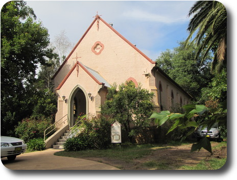 Old brick church, painted cream with brown trim, nicely covered by some trees