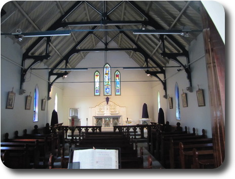 Church interior, white walls, gray roof with dark wooden supports, and dark seats