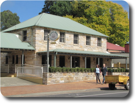 Two storey, square shaped sandstone building with green metal roof