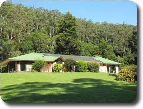 Green lawn leading to house, with tree covered hill behind