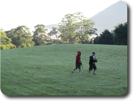 Two little boys walking across frost covered grass, trees in sun behind them