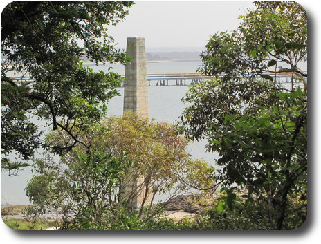 Trees in front of stone obelisk, thence water and part of a long wharf