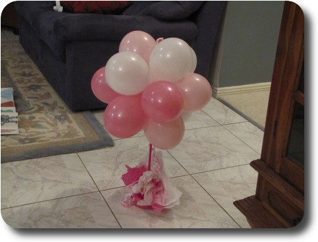 White and pink ballons on a stick in a stand on the floor