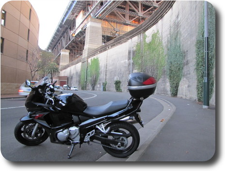 Black motorcycle parked in street with high bridge behind