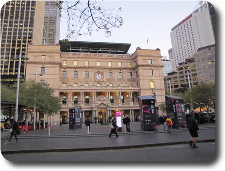 Five storey building, stone facade, plaza in front, high rise buildings on both sides