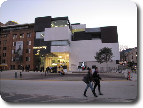 Square building, black and white exterior, adjacent to sandstone building