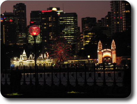 View across water to amusement park at dusk, and tall buildings behind with some lights