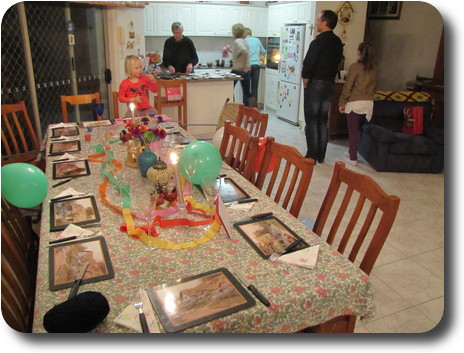 Birthday themed table in foreground, adults in kitchen behind, serving a meal