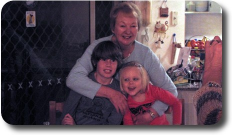 Lady standing behind grandchildren and hugging them as a pair