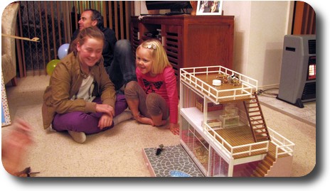 Doll house in foreground, two little girls laughing together