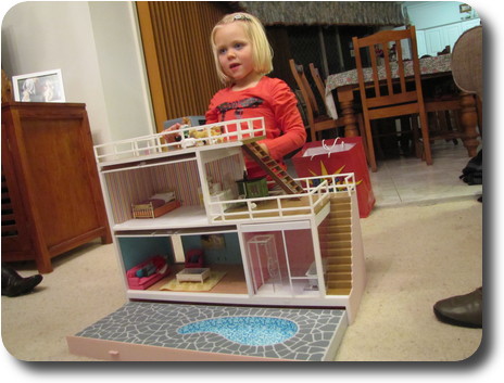 Little girl behind two storey doll house, with swimming pool (no water)