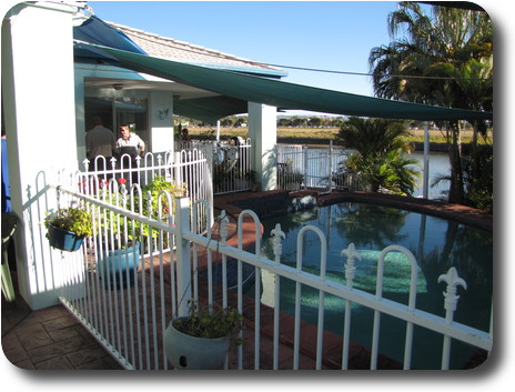 Swimming pool, covered patio and waterway beyond, vacant land further back