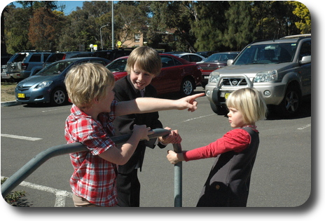 Two little boys and one girl hanging on to railing at edge of car park