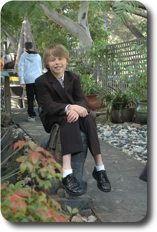 Boy in suit sitting on small stone elephant statue in leafy garden