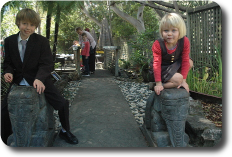 Little boy and little girl sitting on small stone elephant in leafy garden