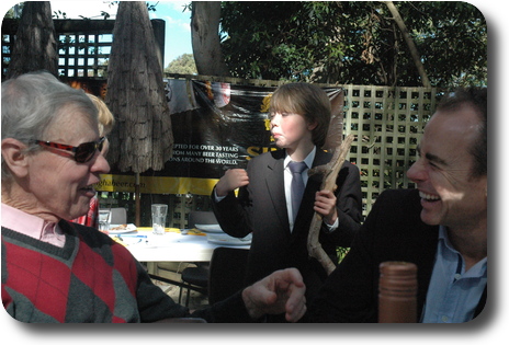 Little boy holding a tree branch, behind two men in conversation