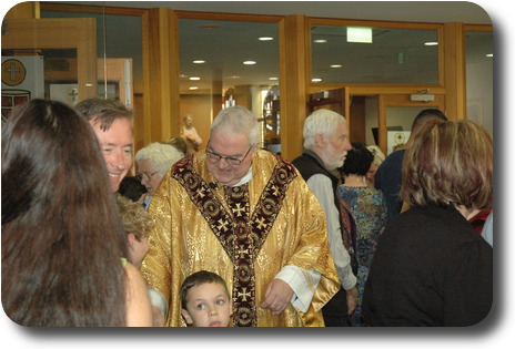 Priest in gold coloured robes with congregation after Mass