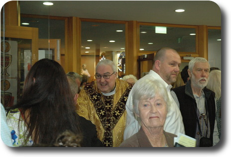 Priest in gold coloured robes with congregation after Mass