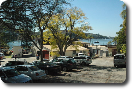 Looking over car park, cream coloured buildings to river and boats, with tree covered hill across the water