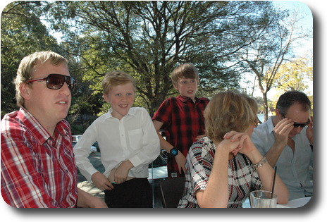 Three adults at table, two boys behind, one in conversation with an adult