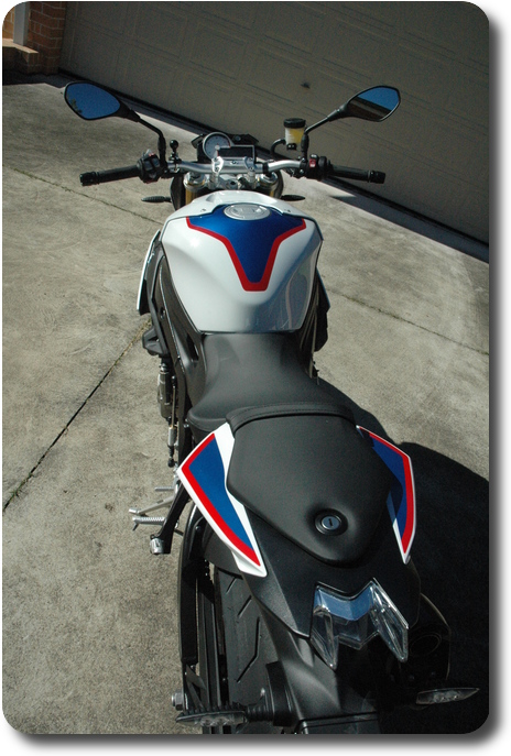 Rear to front view of white, blue red motorcycle, black frame and seat