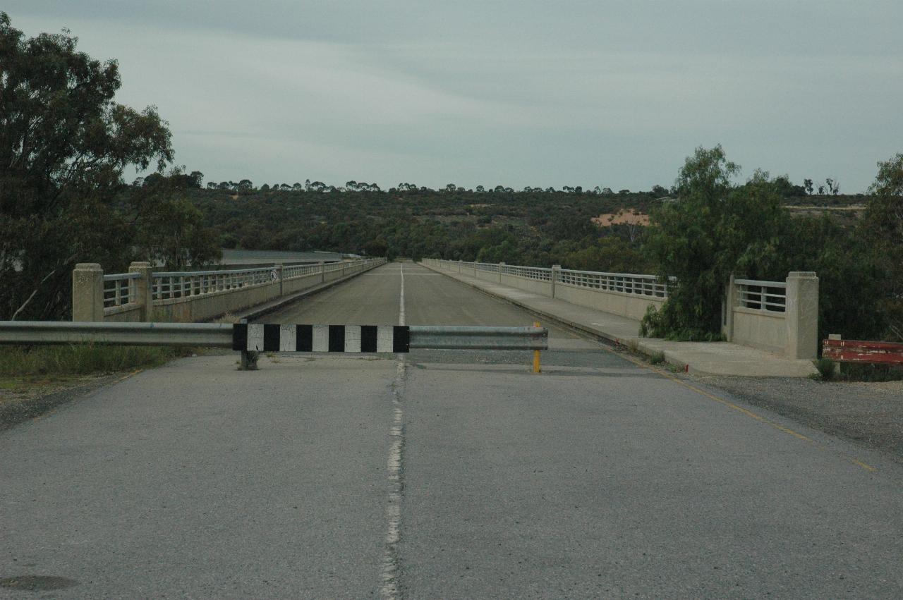 Two lane bridge disappearing in the distance, with barrier to stop vehicles across most of the road.