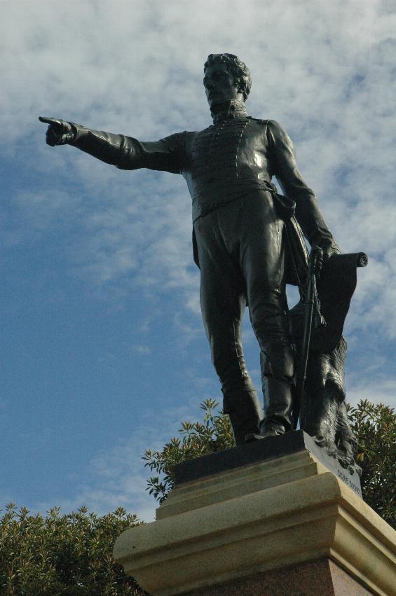 Man on statue, right arm raised, finger points towards Adelaide CBD