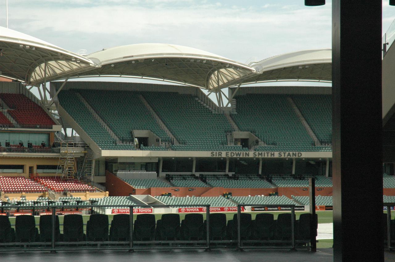 Stands on far side of oval, green or red seats, white scalloped roof in sections over seats