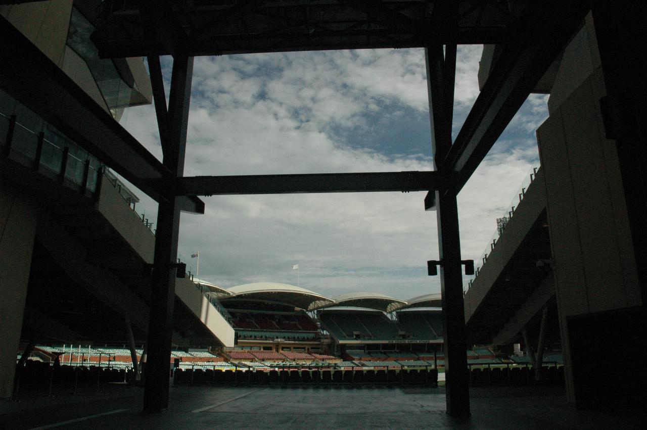View inside from between stands, with steel work in H pattern, to stands with a scalloped white roof in the distance