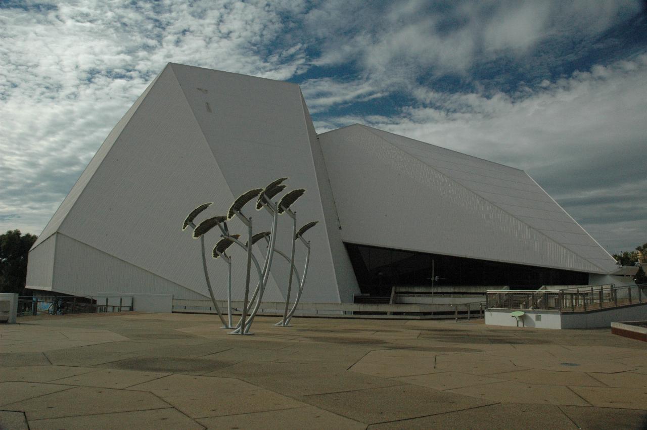 White chunky pyramid style building, with curved metal poles in front and leaf shaped top