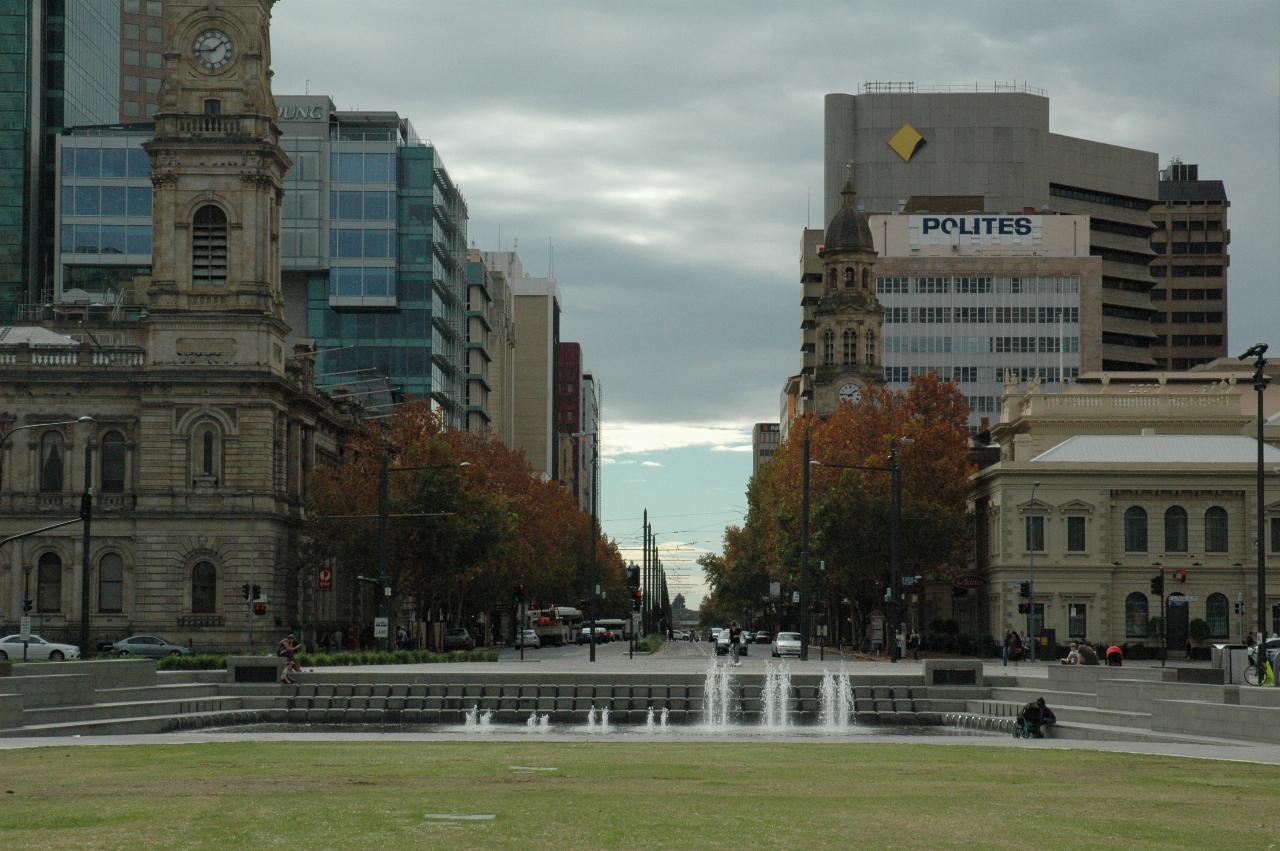 Grassy area with small fountain, looking up street with low and tall buildings