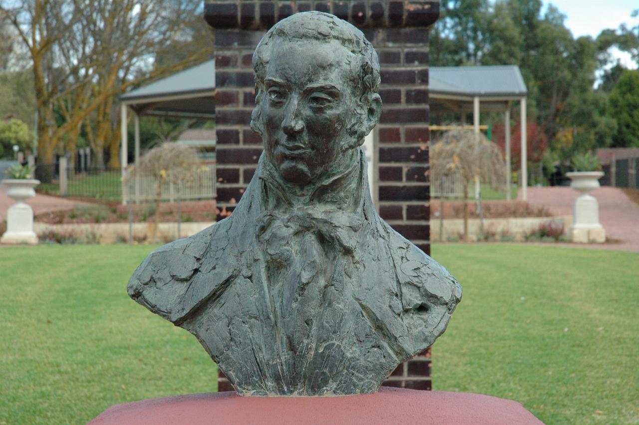 Bust of man sitting on red topped brick pillar