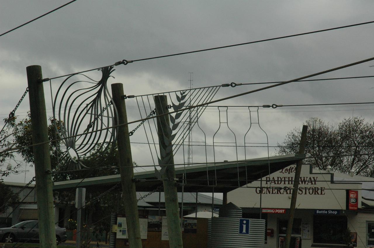 Green wooden poles with wires stretching off and shapes between the pairs of wires, general store in background