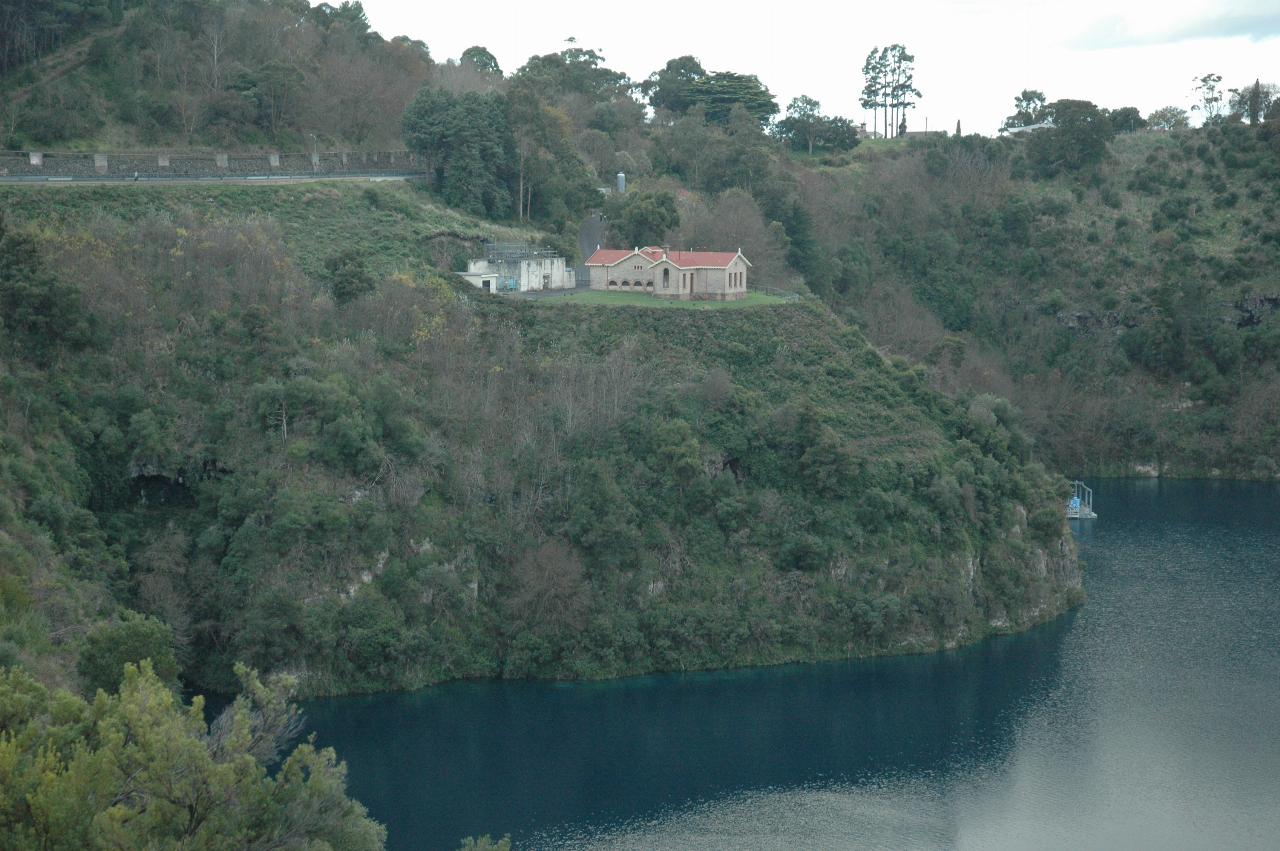 Hill sloping down to water, with an area that has been levelled and contains a cream stone building with a red roof