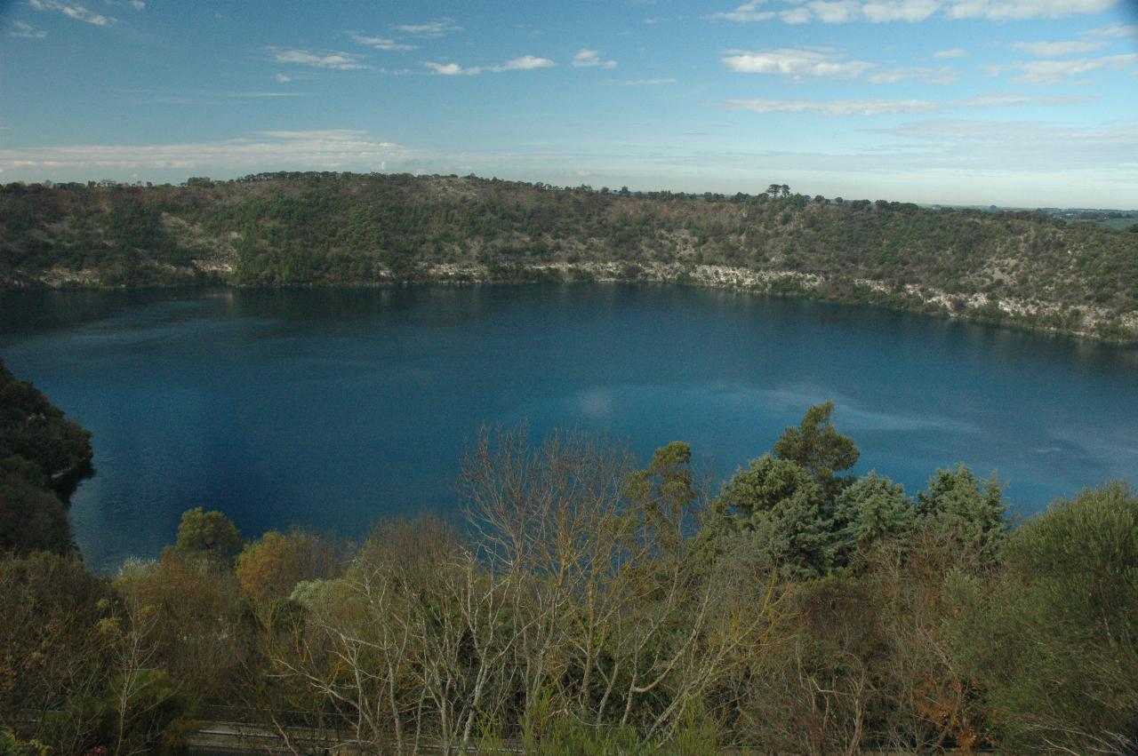 Looking down at volcanic crater with blue water, and white band of rock above the water