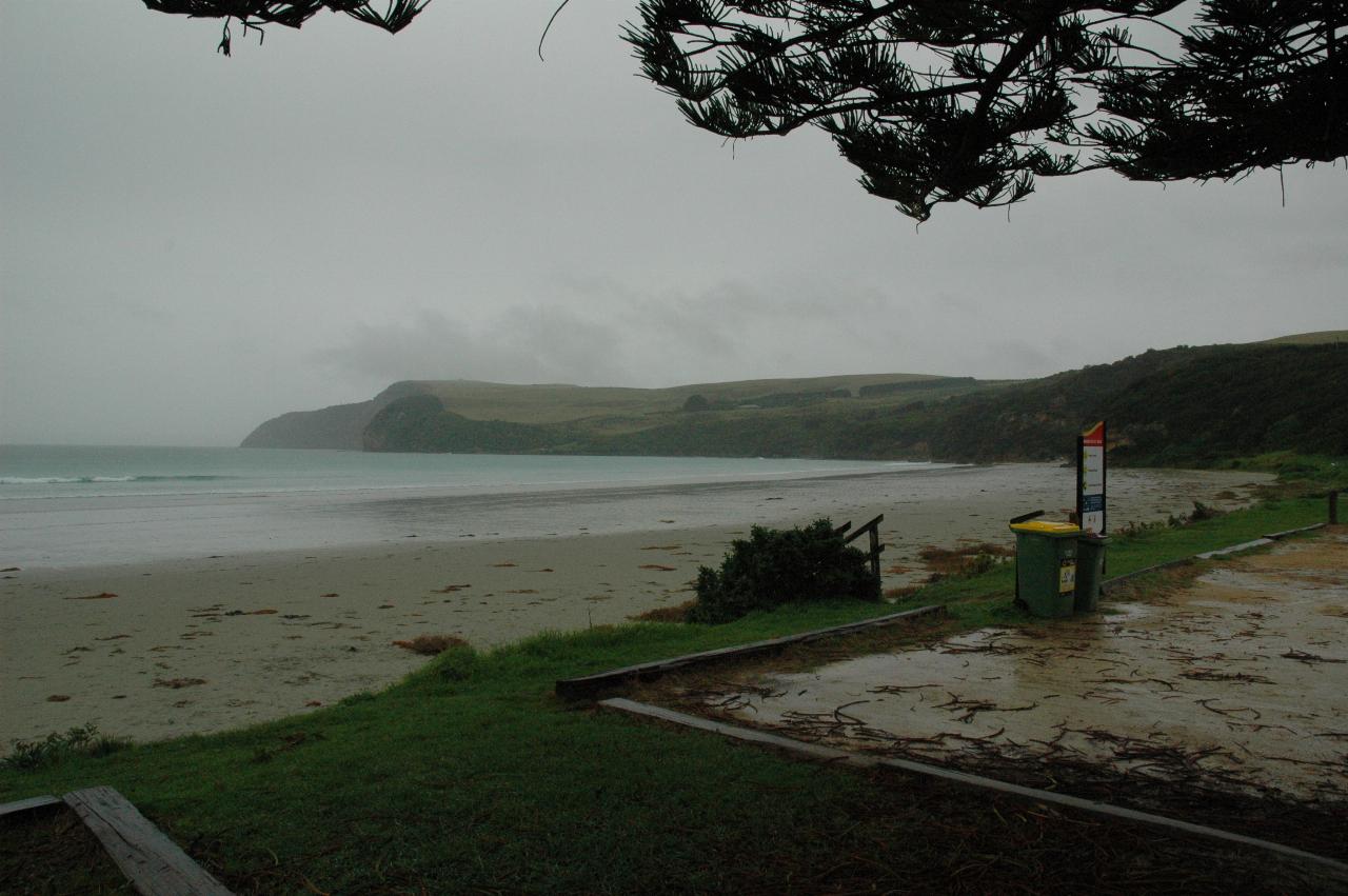 View over sandy beach, gray ocean to headland with gray skies and wet