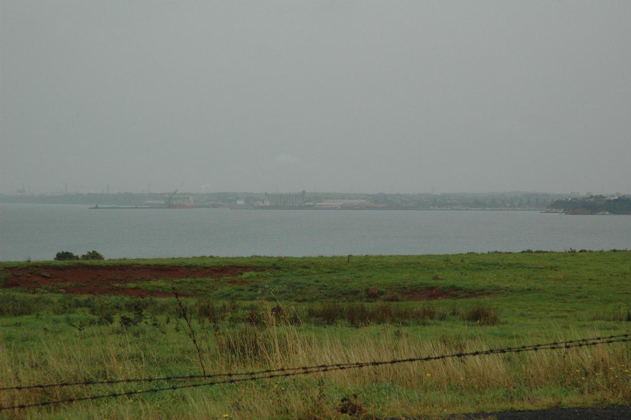 Green field then the ocean and a distant port obscured by rain