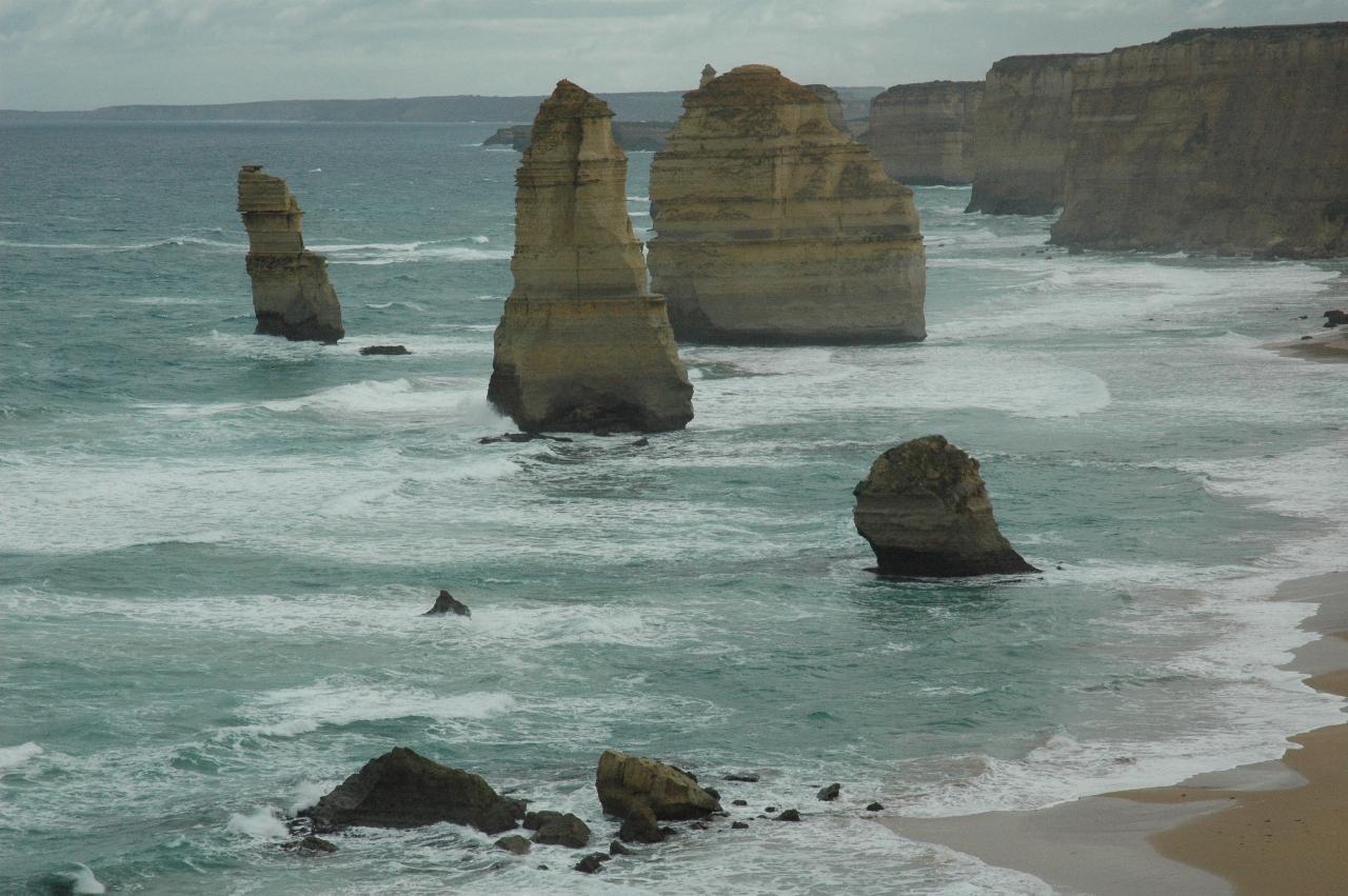 Tall coastal, ochre coloured cliffs with beach and waves, and varied shaped stacks in the ocean
