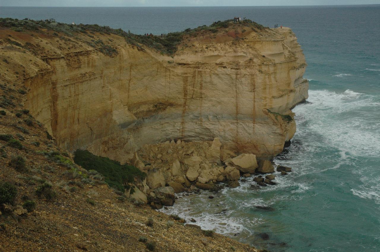 Narrow headland of ochre coloured limestone jutting out to the ocean, with erosion visible on the base